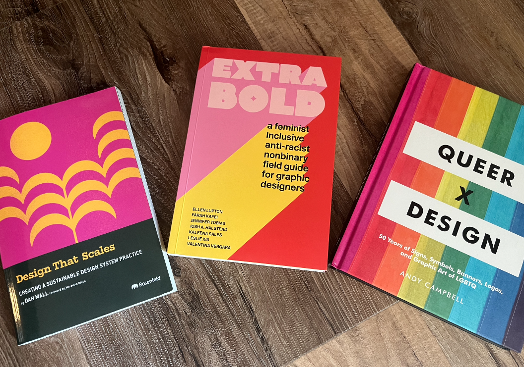 Three vibrant and colorful books, cover-side up, on a wood floor: Design That Scales, Extra Bold, and Queer x Design.