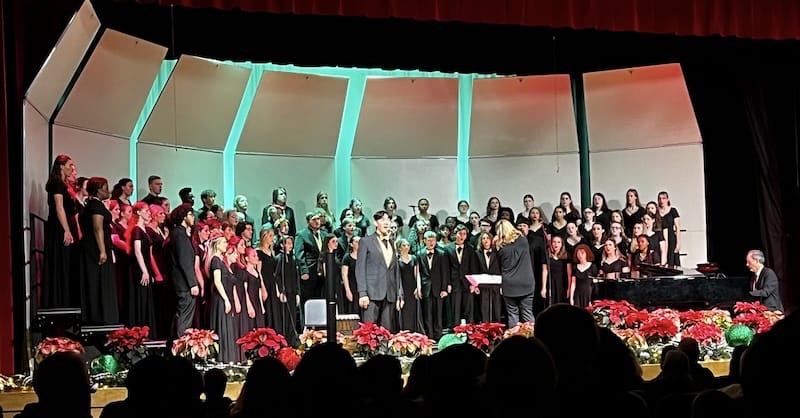 A full choir adorned in green and red lights on a poinsettia-rimmed stage.